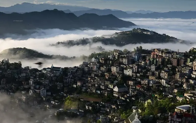 Mizoram’s green hills, traditional houses, and misty landscapes under a clear sky.